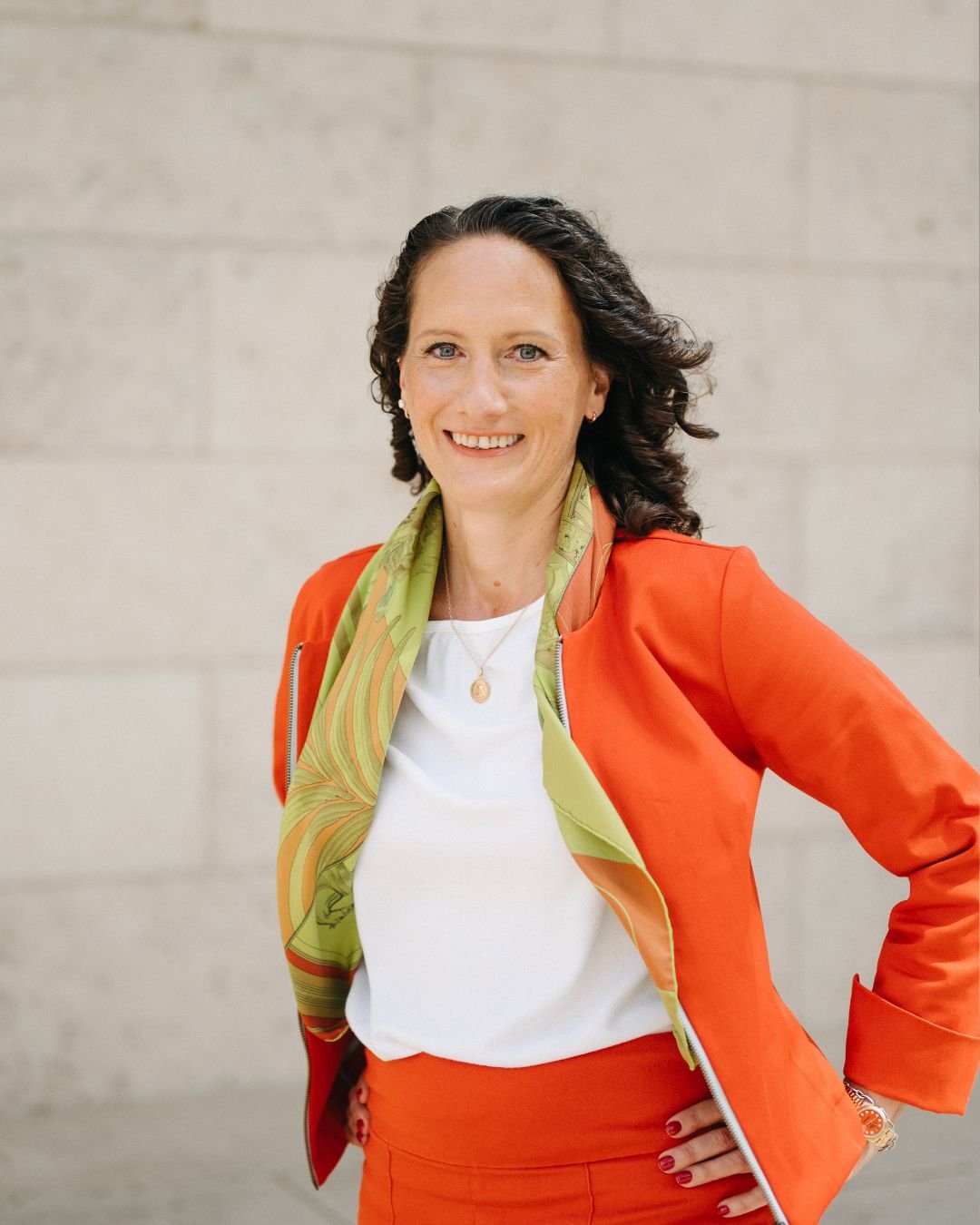 Eine lächelnde Frau mit dunklen, langen Haaren und Brille. Sie lächelt in die Kamera und scheint sich den Betrachter:innen zuzuwenden.